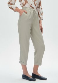 Jasnoszare spodnie elastyczne w talii z kieszeniami bocznymi, mankietami oraz gładką fakturą, zestawione z czarnymi płaskimi butami.