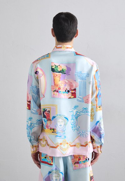 La camicia di seta presenta un collage colorato di motivi artistici classici, tra cui vasi, sculture e cornici ornate, su uno sfondo azzurro chiaro.