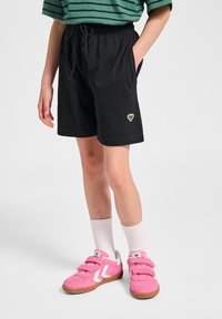 Svarta bomullsshorts med resår i midjan och ficka, med en liten vit logotyp. Matchas med rosa sneakers och vita strumpor.