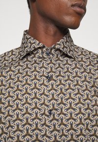 Korte mouw blouse met een geometrisch patroon in marineblauw, crème en bruin. Voorzien van knoopsluiting en een omgeslagen kraag met een gladde textuur.