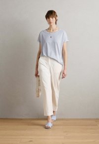 Světle modré tričko s krátkým rukávem, krémové texturované kalhoty a světle modré sandály na klínku. Jednoduchý design s minimem akcentů.
