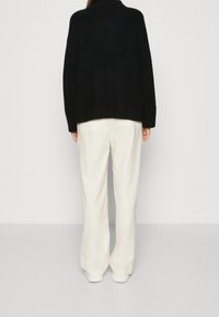 Schwarze Strickjacke mit legerem Schnitt, mit überschnittenen Schultern und gerippter Textur, kombiniert mit cremefarbenen weiten Hosen und weißen Sneakern.