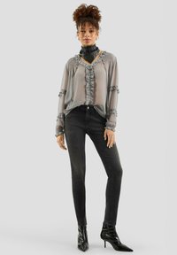 Jasnoszara bluzka z szyfonu z falbankami i czarne wąskie jeansy. Modelka ma na sobie czarne botki na obcasie i czarny choker.