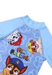 Camisa de manga corta de color azul claro, con personajes de dibujos animados de "Paw Patrol" sobre un fondo azul claro con un patrón de burbujas.