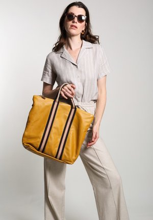 Sac fourre-tout en cuir jaune avec des rayures horizontales noires et rouges, doté de poignées robustes et d'une forme structurée.