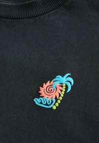 Black fabric t-shirt featuring a colorful embroidered design: a pink spiral flower, teal palm leaves, and green dots, with wavy accents.