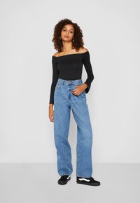 Black off-the-shoulder long-sleeve top paired with high-waisted light blue jeans and black sneakers featuring white accents.