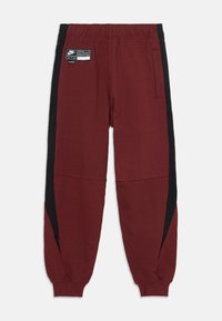Bordo treniņbikses ar melniem sānu paneļiem, elastīgu jostasvietu, smalku tekstūru un mazu Nike Air etiķeti augšējā priekšpusē.