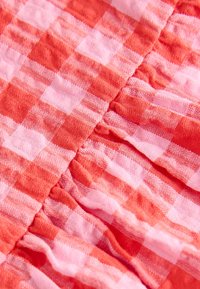 Primo piano di tessuto a quadretti rossi e rosa con cuciture visibili e texture arricciata e stropicciata.