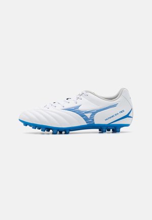 Botas de fútbol blancas con acentos azules, que cuentan con una parte superior texturizada, sistema de cordones y suela con múltiples tacos para tracción.