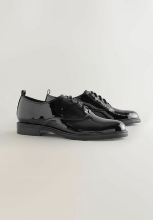 Schwarze Lackleder-Oxford-Schuhe mit abgerundeten Spitzen, Schnürdesign, flachen Absätzen und glatter, reflektierender Oberfläche. Besitzt eine minimalistische Ästhetik.
