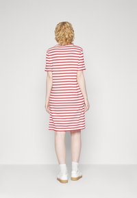 Robe à manches courtes rayée rouge et blanche avec une coupe décontractée, tombant juste au-dessus des genoux. Portée avec des chaussures blanches et des chaussettes.