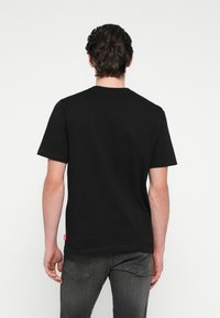 Μαύρο κοντομάνικο μπλουζάκι με στρογγυλή λαιμόκοψη, κατασκευασμένο από βαμβάκι. Διαθέτει μια μικρή κόκκινη ετικέτα λογότυπου στο κάτω μέρος. Απλό σχέδιο, χωρίς σχέδια.