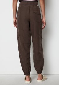 Braune Cargo-Hosen mit elastischem Bund, schmal zulaufenden Knöcheln und zwei Seitentaschen. Hergestellt aus leichtem Stoff mit glatter Textur.