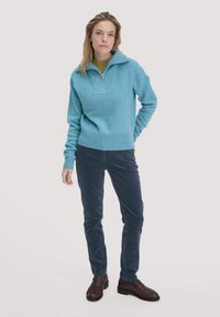 Hellblauer Pullover mit Reißverschluss und strukturiertem Stoff, kombiniert mit dunkelblauen Cordhosen und braunen Schuhen. Wichtige Details sind gerippte Bündchen und Saum.