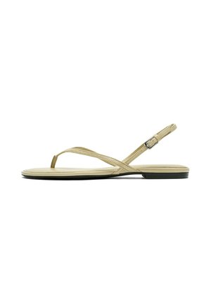 Sandale plate beige avec fines lanières, une boucle d’orteil et une bride de cheville réglable avec une petite boucle.