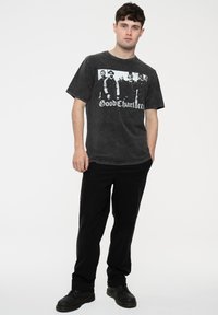 Black graphic t-shirt with a faded distressed look, featuring a white print of figures and "Good Charlotte" text. Paired with black pants and footwear.