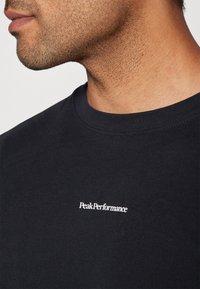 T-shirt nera in cotone con scollo rotondo. Presenta il logo bianco "PeakPerformance" ricamato sul petto. Texture morbida.