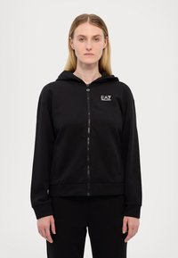 Felpa nera con zip e cappuccio, realizzata in tessuto morbido. Presenta un piccolo logo EA7 bianco sul petto a sinistra e tasche laterali.