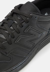 Black athletic shoe made of synthetic leather with a textured surface, featuring black laces and an embossed logo on the side.