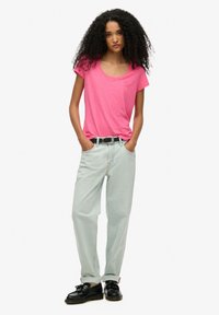 Camisa de manga corta de color rosa brillante, jeans holgados de color azul claro y zapatos negros. El atuendo incluye un cinturón con una hebilla de plata.