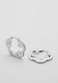 Silberfarbener Ring in Wolkenform, verziert mit klaren Strasssteinen entlang der Ränder und drei zentralen Steinen. Glatte metallische Textur.