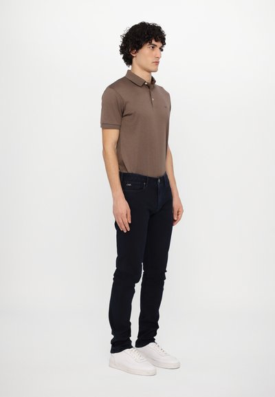 Brown polo shirt with a collar, short sleeves, paired with dark blue jeans and white sneakers. Simple design with no visible patterns.