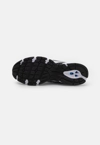 Czarna gumowa podeszwa z wzorzystym bieżnikiem, z białymi akcentami i niebieskim detalem. Zaprojektowana dla przyczepności i trwałości podczas aktywności sportowych.