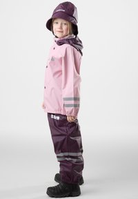 Pink waterproof jacket with gray reflective stripes and buttons, paired with dark purple waterproof pants, and a matching purple bucket hat.