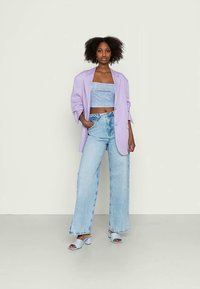 Blazer oversized em lilás, top cortado cinza, jeans de perna larga em azul claro e mules de salto em azul claro. Texturas suaves e ajuste relaxado.