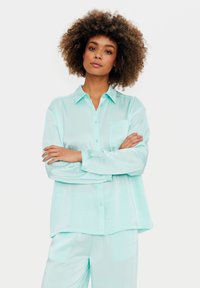 Camicia azzurro menta a maniche lunghe con bottoni, dal tessuto liscio, dotata di taschino sul petto e vestibilità comoda. Si abbina a pantaloni menta coordinati.