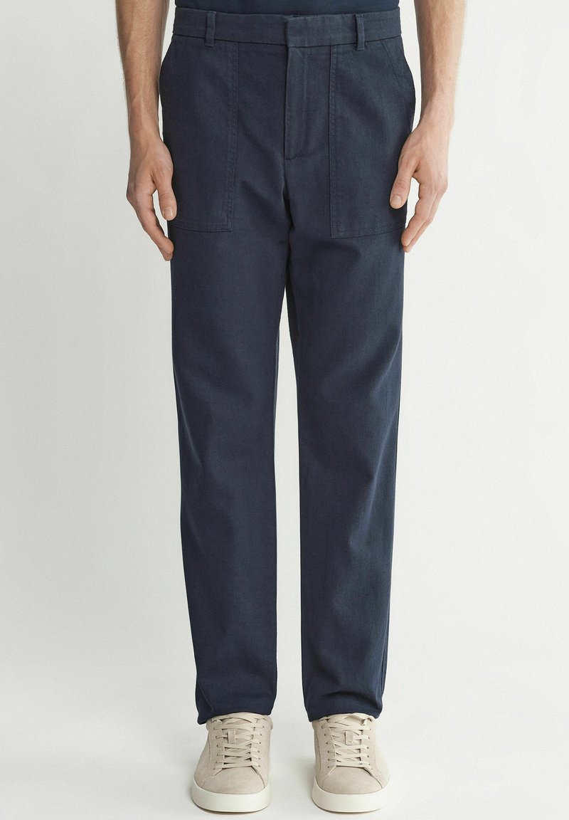 Marinblå bomullsbukser med rak ben-design, utrustad med två framfickor och stylad med ljusa skor.