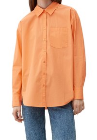 Langærmet skjorte med krave i ensfarvet orange bomuld med en brystlomme, featuring knaplukning foran og afslappet pasform. Sammen med blå jeans.
