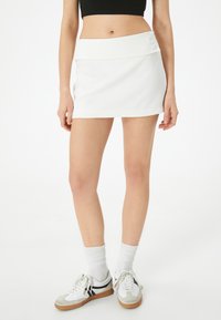 Witte mini-rok met een brede tailleband, een vlakke voorkant en twee ronde knopen. Glad textuur en een aansluitend ontwerp. G gedragen met casual sneakers.