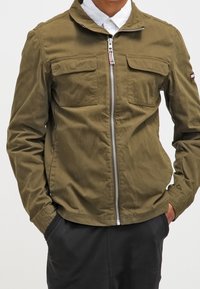 Olive green jacket with a zippered front, two chest pockets, and a stand-up collar. Fabric appears lightweight and smooth.
