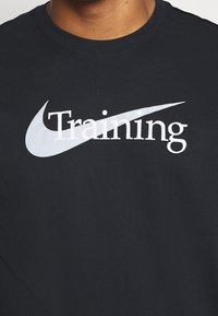 Schwarzes Nike-T-Shirt mit fett gedrucktem weißen "Training"-Text und dem Nike-Swoosh-Logo, aus weichem Stoff mit Rundhalsausschnitt.