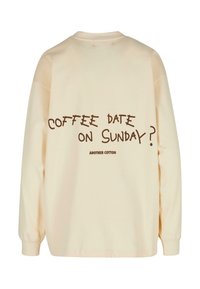 Sweat-shirt à manches longues couleur crème avec un texte graphique marron au dos qui dit "RENDEZ-VOUS CAFÉ LE DIMANCHE ?" et une coupe décontractée.