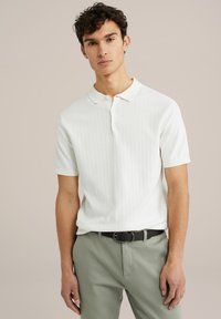 Polo alb cu mânecă scurtă, cu textură ribbed, guler clasic, placket cu butoane, asortat cu pantaloni verzi deschiși și o curea închisă la culoare.