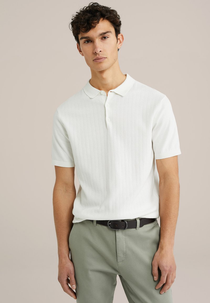 Polo alb cu mânecă scurtă, cu textură ribbed, guler clasic, placket cu butoane, asortat cu pantaloni verzi deschiși și o curea închisă la culoare.