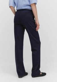 Mörkblå byxor med rak bendesign, med en subtil textur och två bakfickor, tillsammans med svarta platta skor.