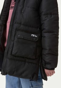 Giacca a vento nera con zip, tasca con bottone e polsini a coste. Presenta un morbido rivestimento interno e un motivo a righe orizzontali imbottito.