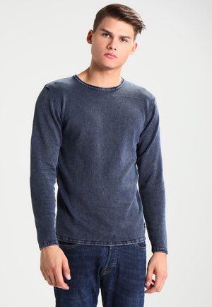 Langarm navyblau shirt met ronde hals van zacht materiaal, met een licht vervaagde textuur en zichtbare stikseldetails. Gekleed met donkere jeans.