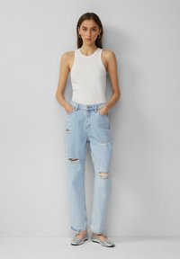 Débardeur blanc à rayures avec des clous argentés, associé à un jean en denim déchiré bleu clair et des chaussures plates argentées.