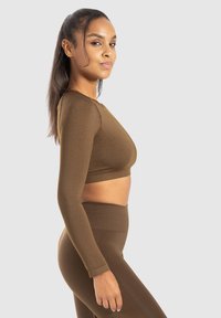 Top crop lungo marrone a maniche lunghe con scollo rotondo, abbinato a leggings a vita alta coordinati, caratterizzati da una texture di tessuto morbido e elastico.