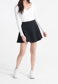Zwarte skaterrok met een gestructureerd oppervlak en een aansluitende tailleband, gecombineerd met een witte lange mouwtop en witte sneakers.