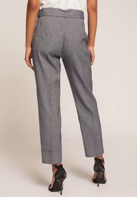 Šedé, texturované kalhoty s přizpůsobeným střihem, s poloviční výškou pasu a s manžetami na nohavicích. V kombinaci s černými lodičkami na vysokém podpatku.