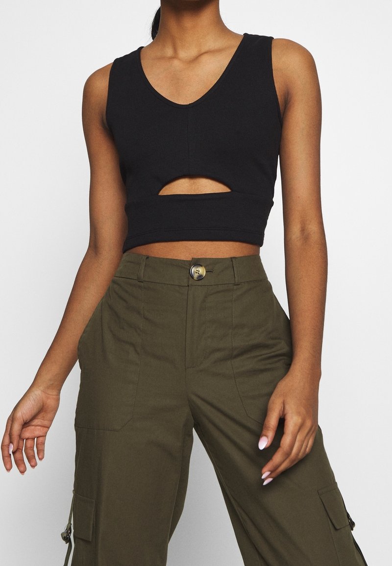 Haut court sans manches noir avec un décolleté en V et un détail découpé à la taille, associé à un pantalon cargo vert olive avec une fermeture à bouton.