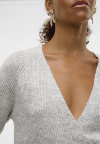 Light gray knitted sweater with a deep V-neck design. Features ribbed texture and raglan sleeves. Earring details visible to the side.