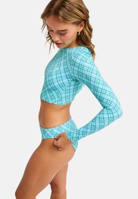 Μπλούζα μαγιό με μακριά μανίκια και ταίριαστο κάτω μέρος σε ανοιχτό μπλε με σχέδιο πλέγματος. Το υλικό είναι λείο και ελαστικό, με εφαρμοστή σχεδίαση και cropped μήκος.