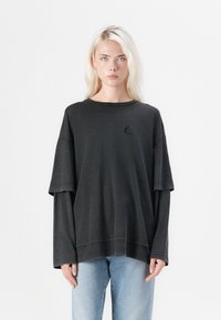Zwarte oversized t-shirt met een ronde halslijn, korte mouwen en gelaagde lange mouwen. Kenmerkt zich door een klein geborduurd zeilbootlogo.